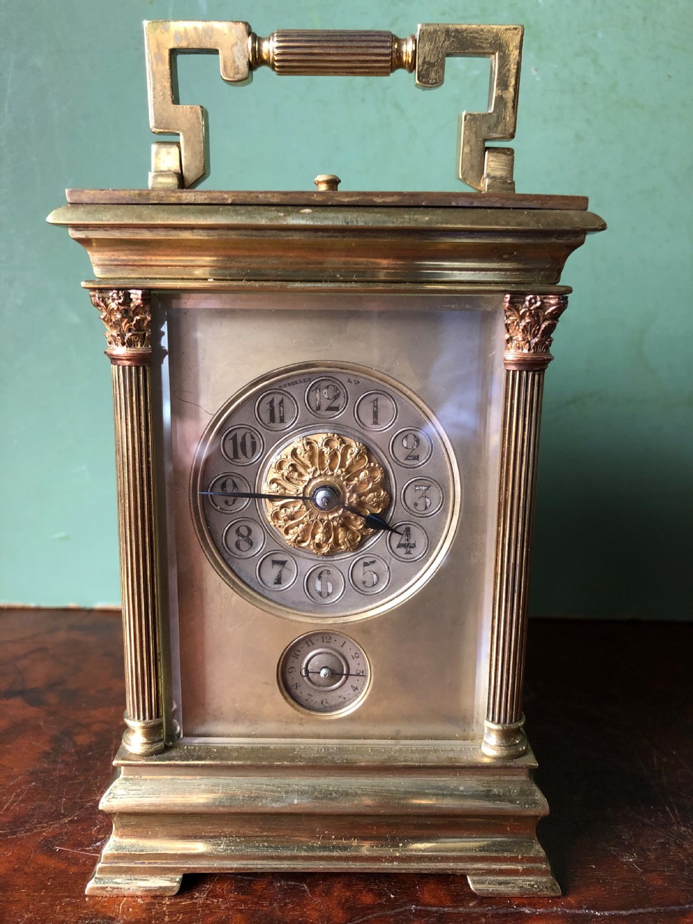 A late nineteenth-century French gilt brass carriage clock featuring fluted Corinthian corner columns, a carrying handle, a central dial with Arabic numerals, a lower subsidiary dial, and an adjacent winding key. View XIX