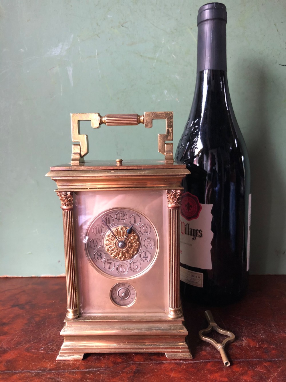 A late nineteenth-century French gilt brass carriage clock featuring fluted Corinthian corner columns, a carrying handle, a central dial with Arabic numerals, a lower subsidiary dial, and an adjacent winding key. View XX