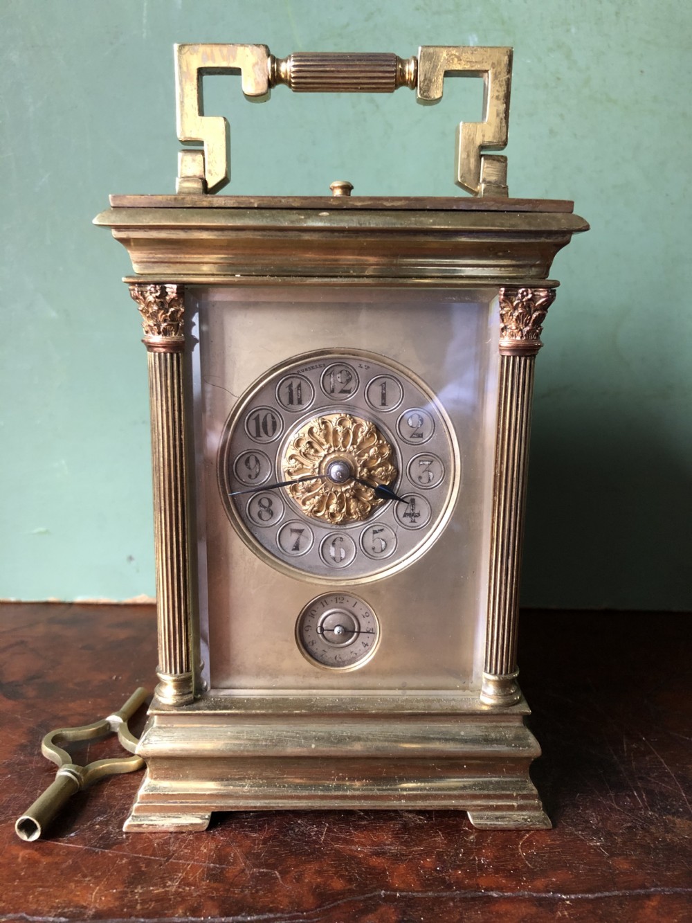 A late nineteenth-century French gilt brass carriage clock featuring fluted Corinthian corner columns, a carrying handle, a central dial with Arabic numerals, a lower subsidiary dial, and an adjacent winding key. View XXII