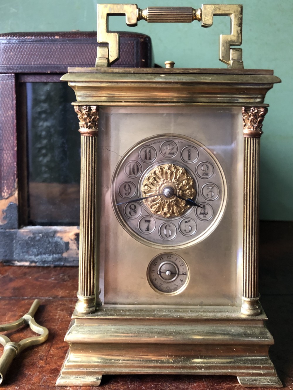 A late nineteenth-century French gilt brass carriage clock featuring fluted Corinthian corner columns, a carrying handle, a central dial with Arabic numerals, a lower subsidiary dial, and an adjacent winding key. View V