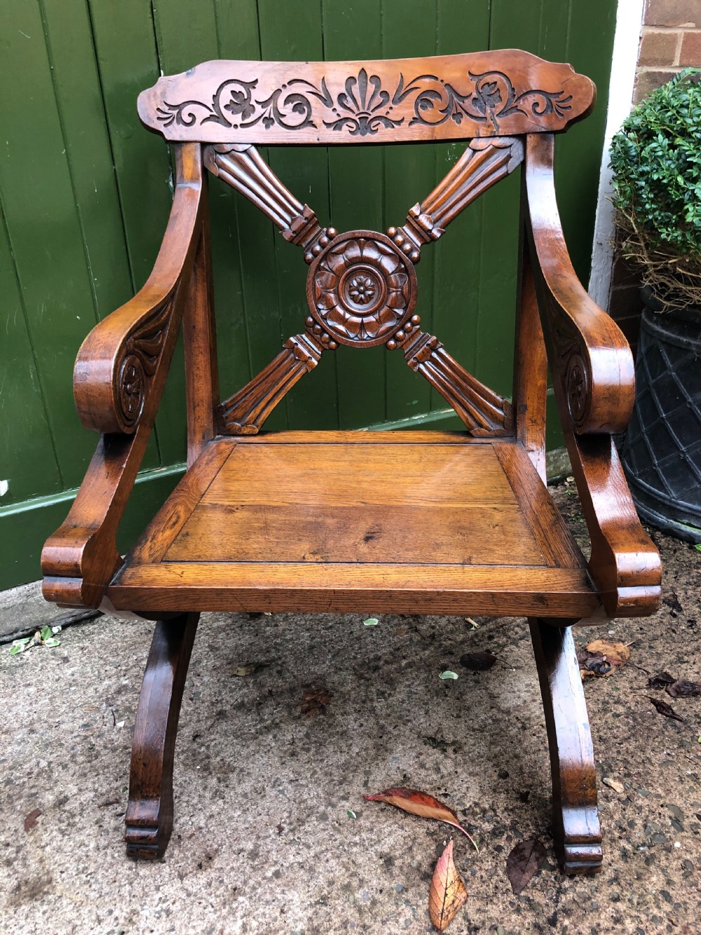 A nineteenth-century carved oak armchair featuring an X-frame back with a central rosette, scrolled armrests, and curved legs.