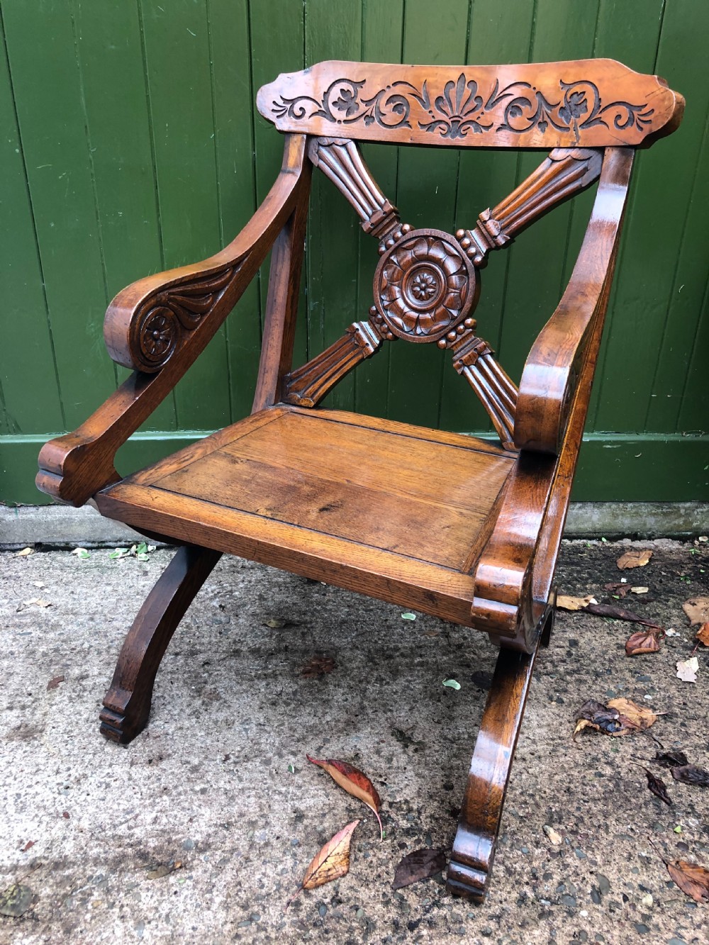 A nineteenth-century carved oak armchair featuring an X-frame back with a central rosette, scrolled armrests, and curved legs. View II