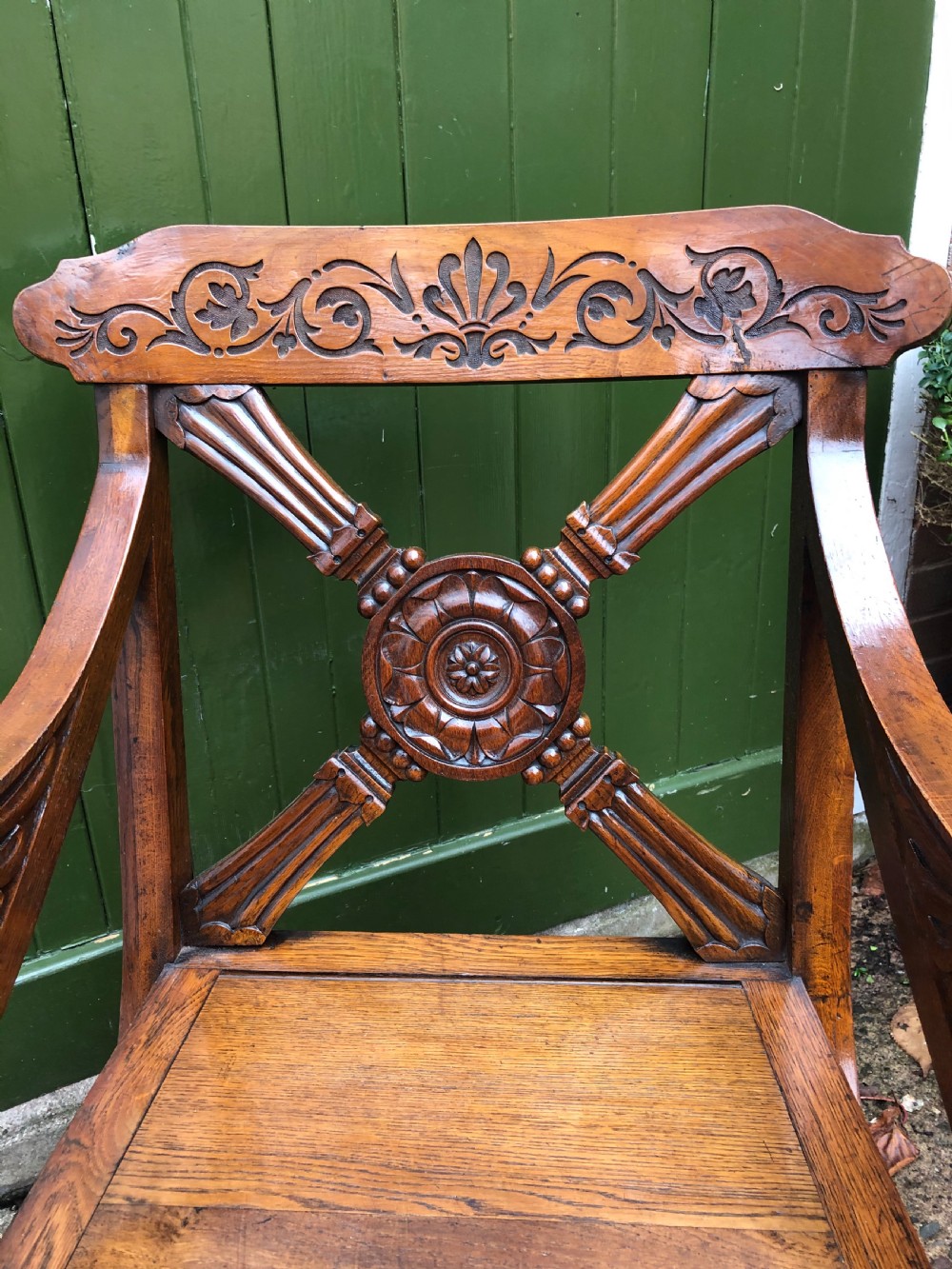A nineteenth-century carved oak armchair featuring an X-frame back with a central rosette, scrolled armrests, and curved legs. View III
