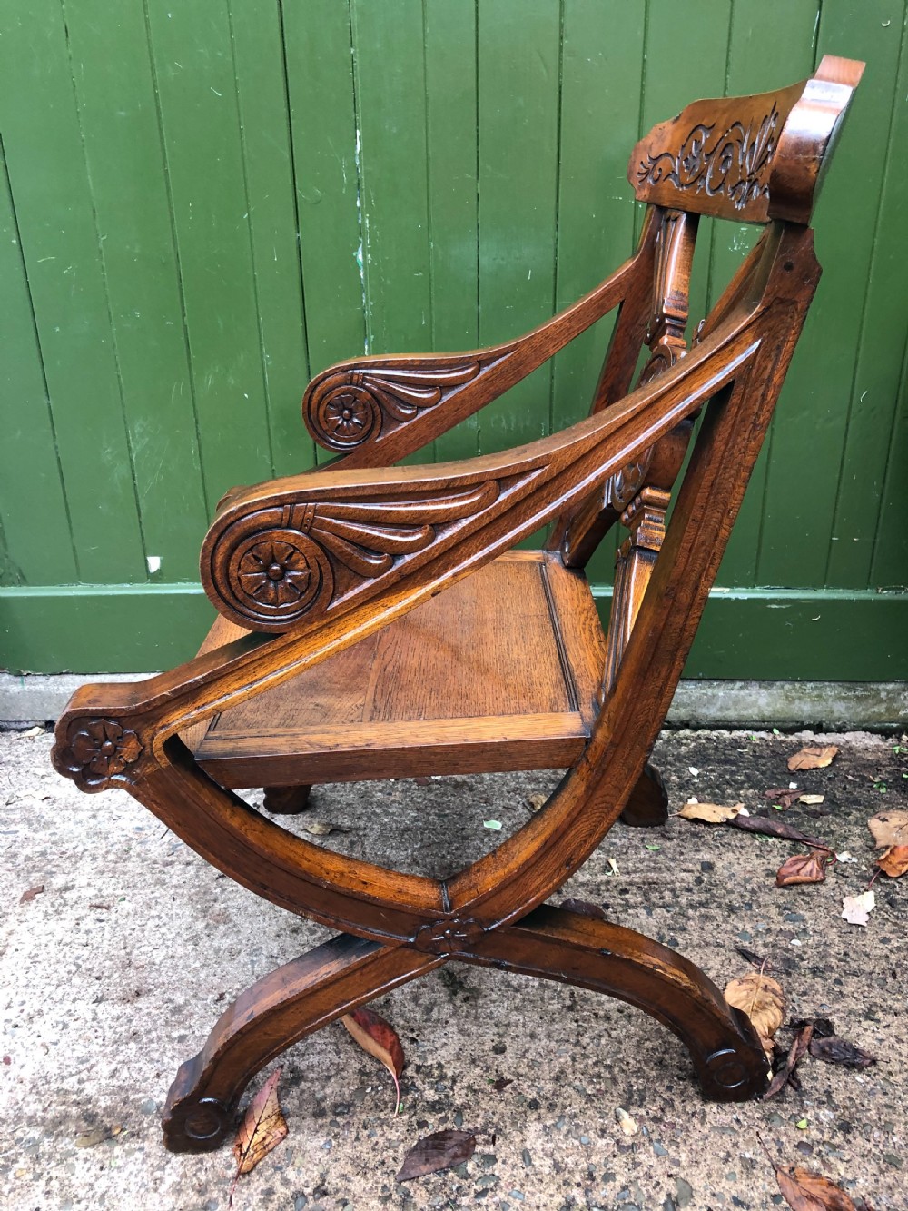 A nineteenth-century carved oak armchair featuring an X-frame back with a central rosette, scrolled armrests, and curved legs. View IV