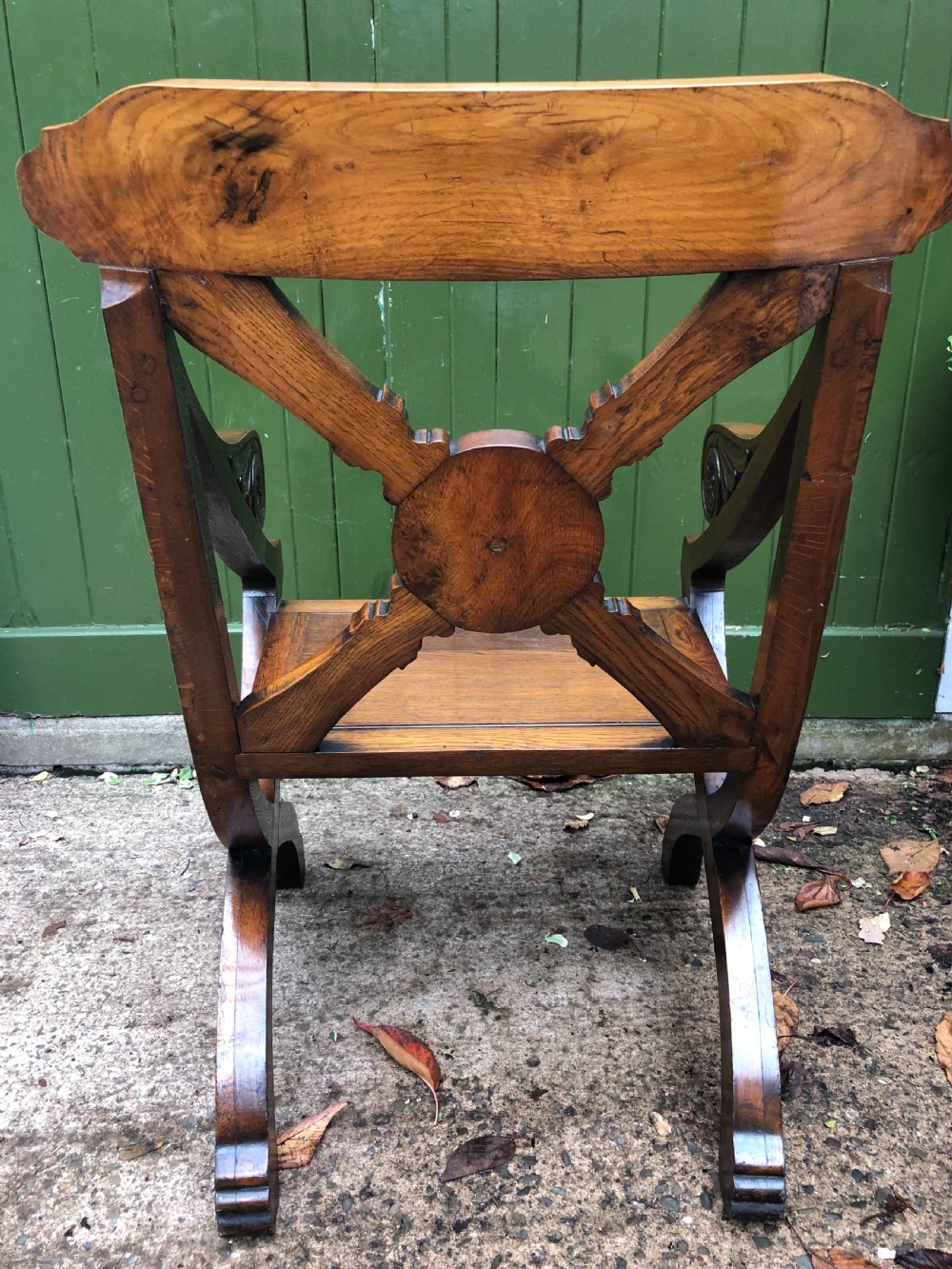 A nineteenth-century carved oak armchair featuring an X-frame back with a central rosette, scrolled armrests, and curved legs. View V