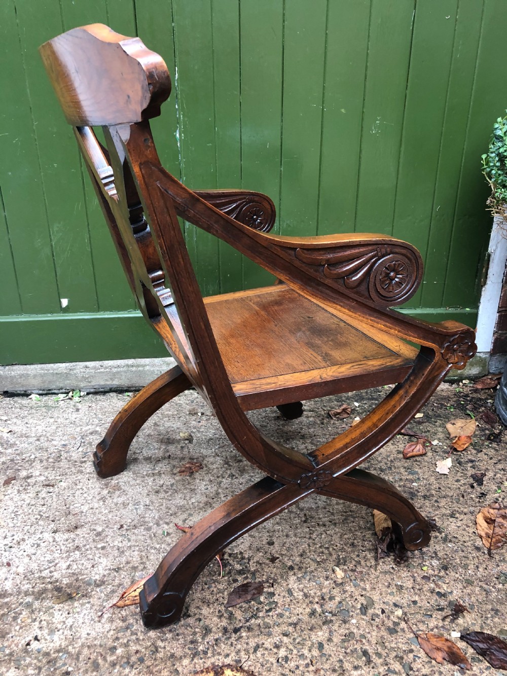 A nineteenth-century carved oak armchair featuring an X-frame back with a central rosette, scrolled armrests, and curved legs. View VI