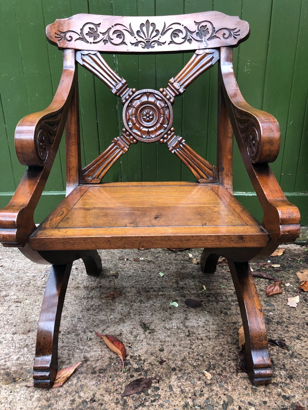 A nineteenth-century carved oak armchair featuring an X-frame back with a central rosette, scrolled armrests, and curved legs. View IX