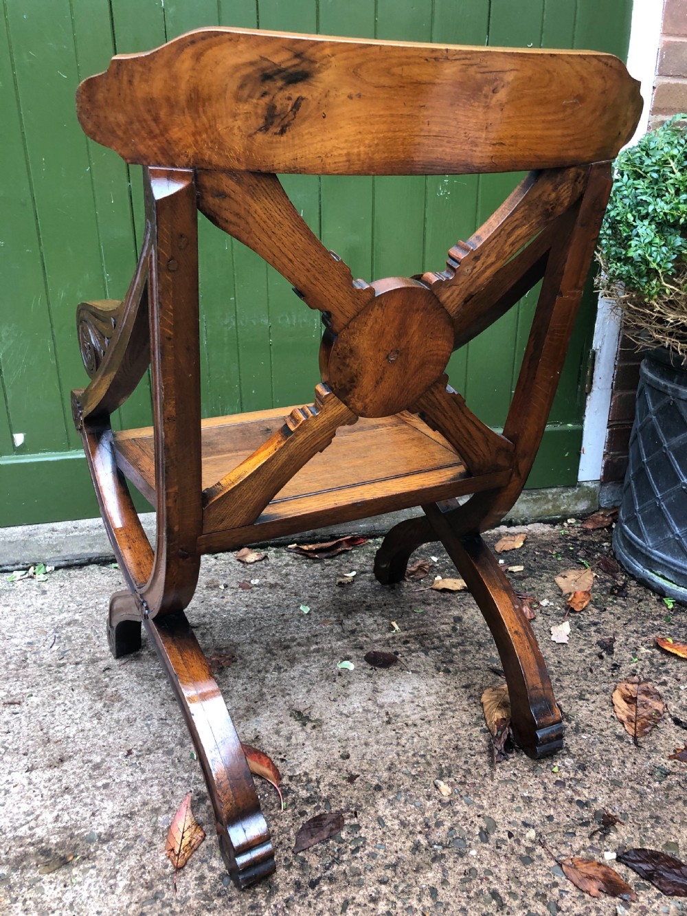 A nineteenth-century carved oak armchair featuring an X-frame back with a central rosette, scrolled armrests, and curved legs. View X