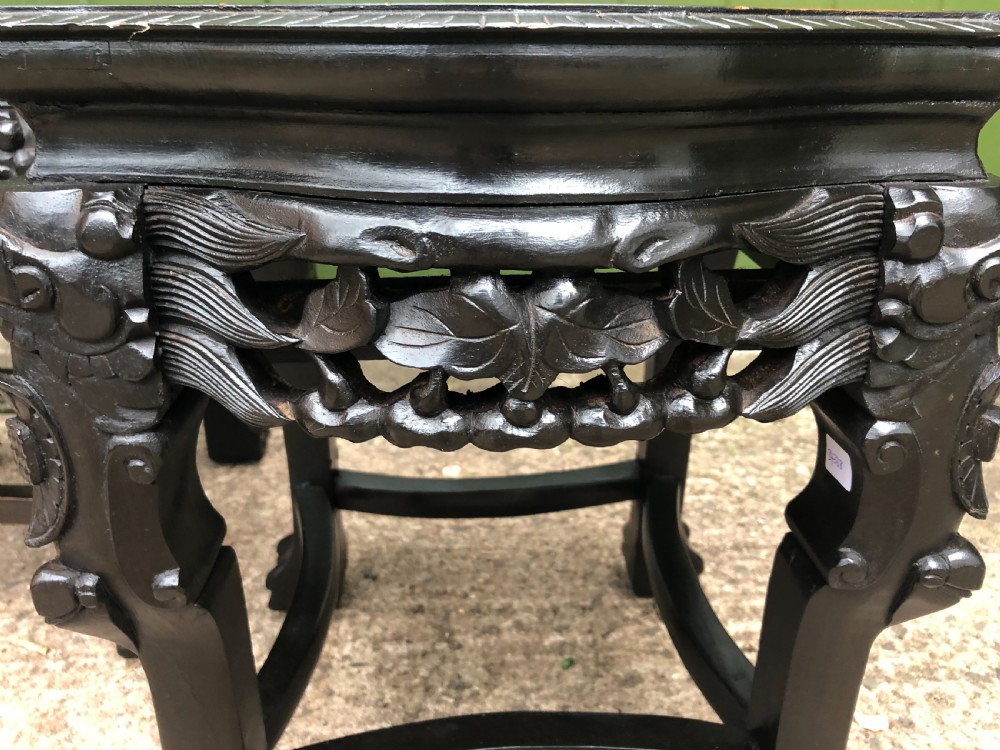 Pair of ebonised wooden side tables featuring pierced floral carvings and circular pink marble inset tops. View X