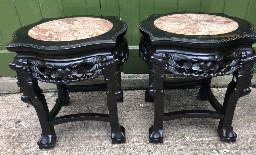 Pair of ebonised wooden side tables featuring pierced floral carvings and circular pink marble inset tops.