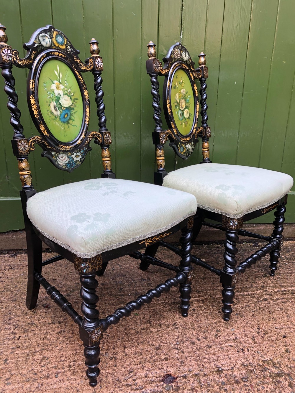 A pair of black lacquered Victorian bedroom chairs featuring oval back panels painted with floral motifs, mother-of-pearl inlay, barley twist legs, and light green upholstered seats. View VI