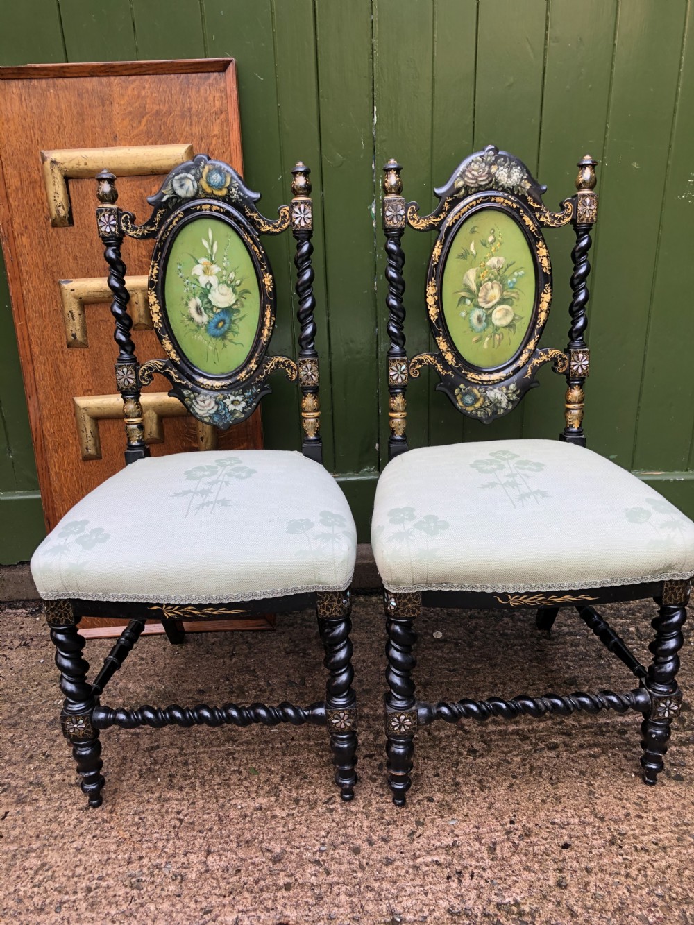 A pair of black lacquered Victorian bedroom chairs featuring oval back panels painted with floral motifs, mother-of-pearl inlay, barley twist legs, and light green upholstered seats. View XVI