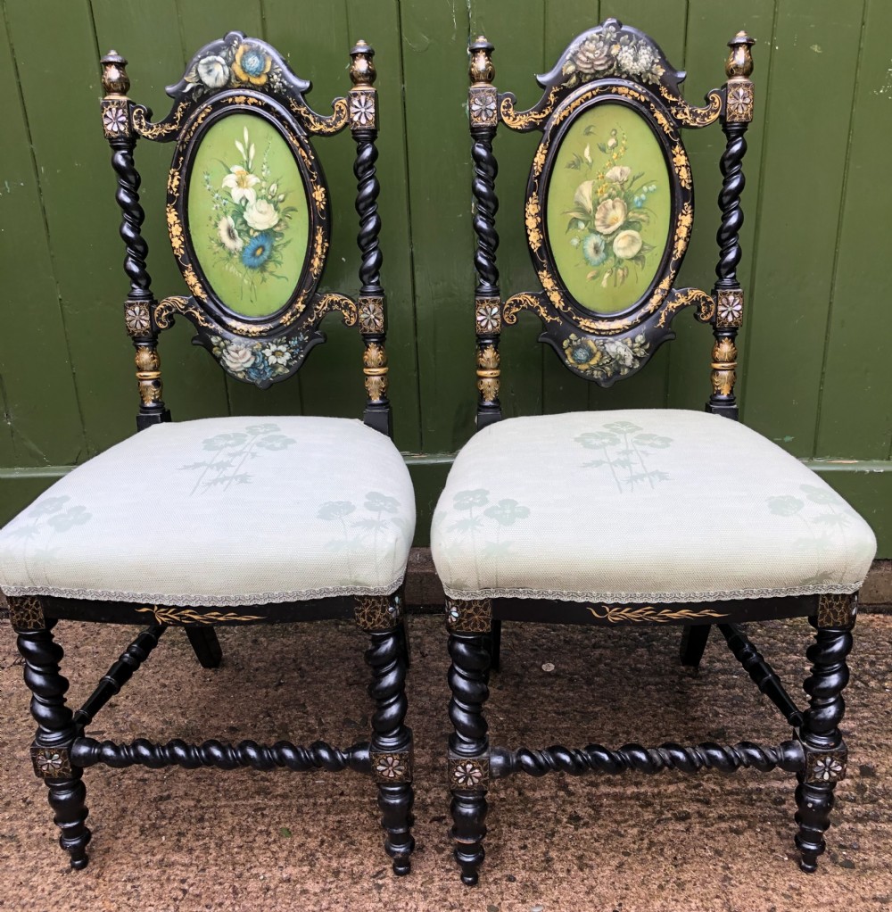 A pair of black lacquered Victorian bedroom chairs featuring oval back panels painted with floral motifs, mother-of-pearl inlay, barley twist legs, and light green upholstered seats.