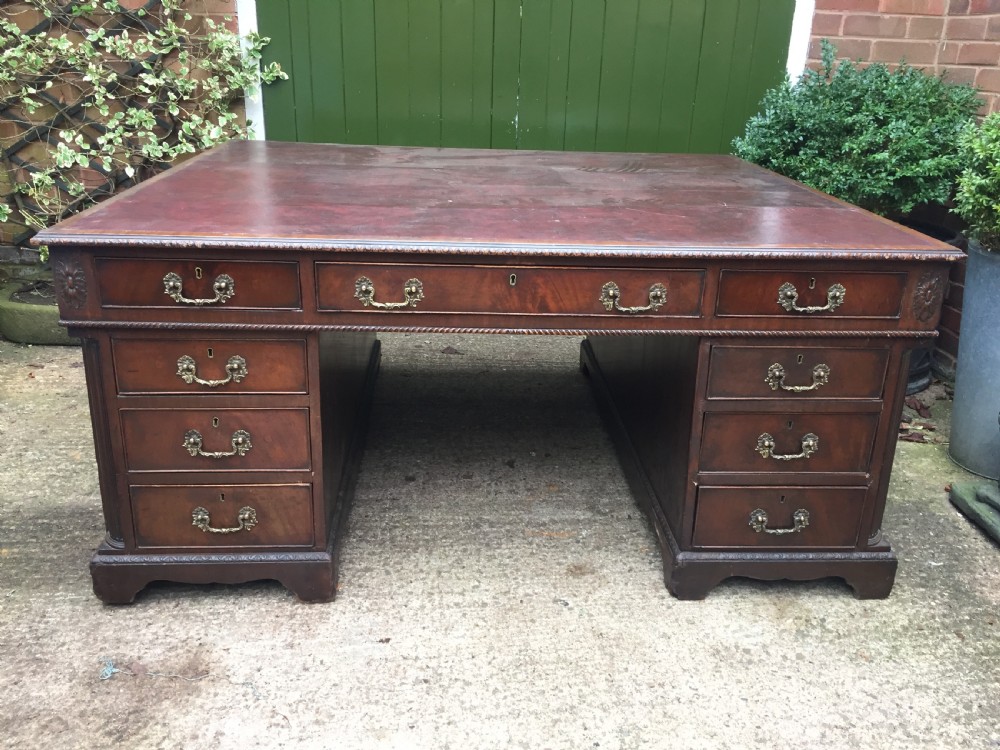 A nineteenth-century Chippendale-revival mahogany partners desk featuring an inset leather top, twin pedestals with drawer storage, brass handles, and carved edge trim. View VII
