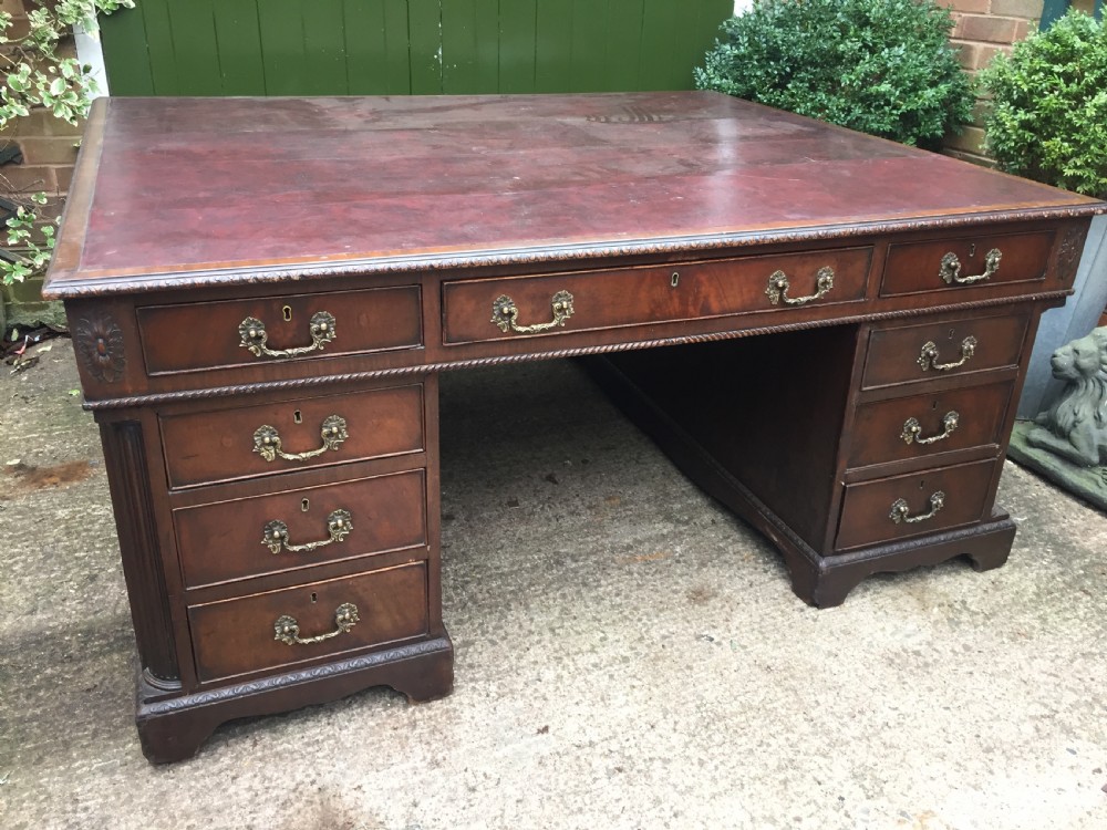 A nineteenth-century Chippendale-revival mahogany partners desk featuring an inset leather top, twin pedestals with drawer storage, brass handles, and carved edge trim. View VIII