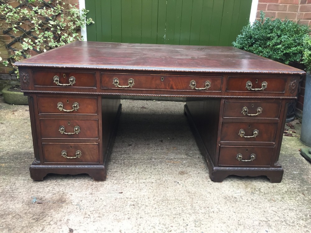A nineteenth-century Chippendale-revival mahogany partners desk featuring an inset leather top, twin pedestals with drawer storage, brass handles, and carved edge trim. View XI