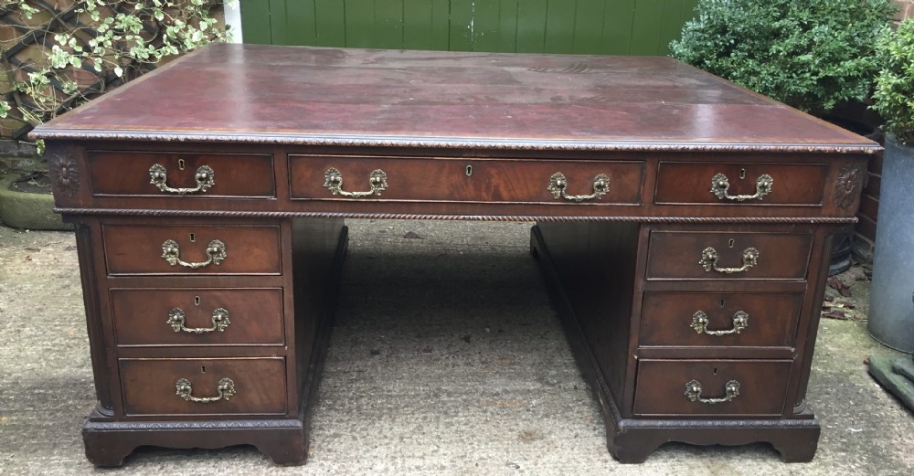 A nineteenth-century Chippendale-revival mahogany partners desk featuring an inset leather top, twin pedestals with drawer storage, brass handles, and carved edge trim.