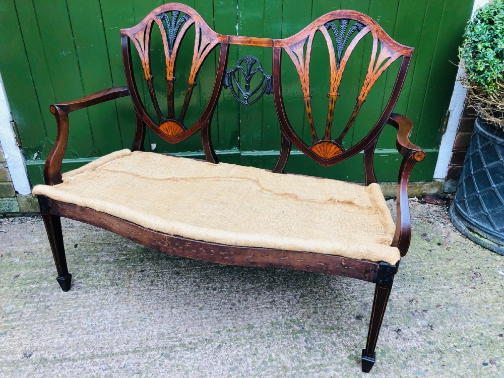 A late nineteenth-century mahogany double chair-back settee featuring shield-shaped backs with satinwood plume inlay and tapered legs.