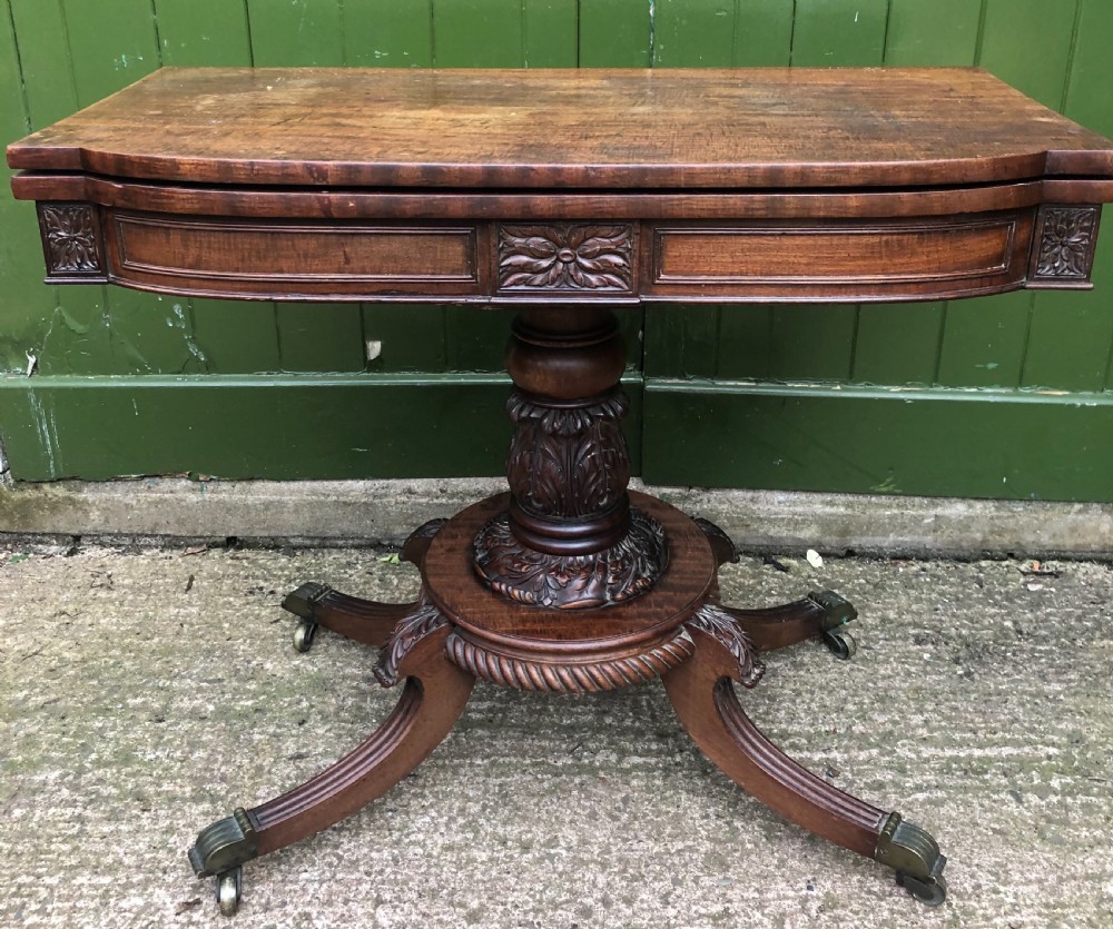 An early 19th-century Regency mahogany fold-over card table featuring carved floral frieze panels, a bulbous carved pedestal stem, and four splayed legs with brass castors. View III