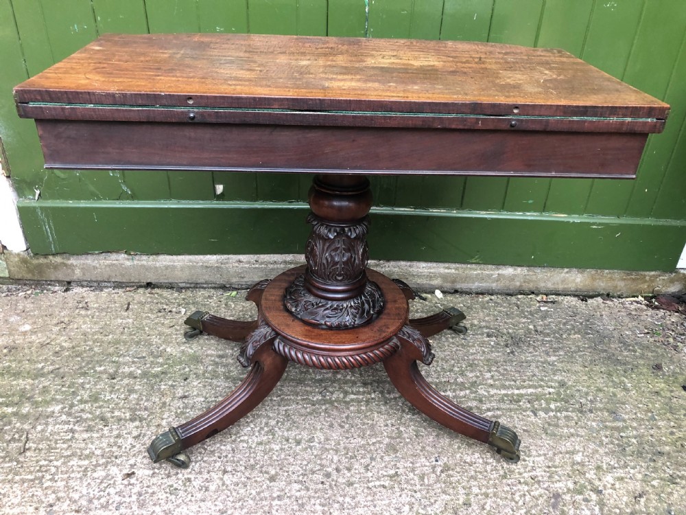 An early 19th-century Regency mahogany fold-over card table featuring carved floral frieze panels, a bulbous carved pedestal stem, and four splayed legs with brass castors. View VI