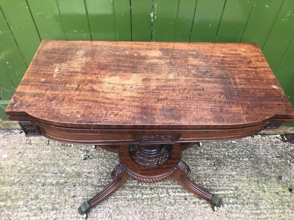 An early 19th-century Regency mahogany fold-over card table featuring carved floral frieze panels, a bulbous carved pedestal stem, and four splayed legs with brass castors. View XIII