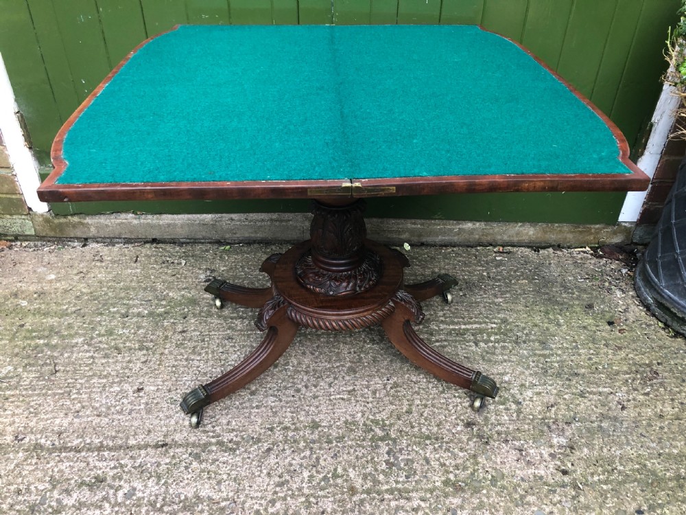 An early 19th-century Regency mahogany fold-over card table featuring carved floral frieze panels, a bulbous carved pedestal stem, and four splayed legs with brass castors. View XVI