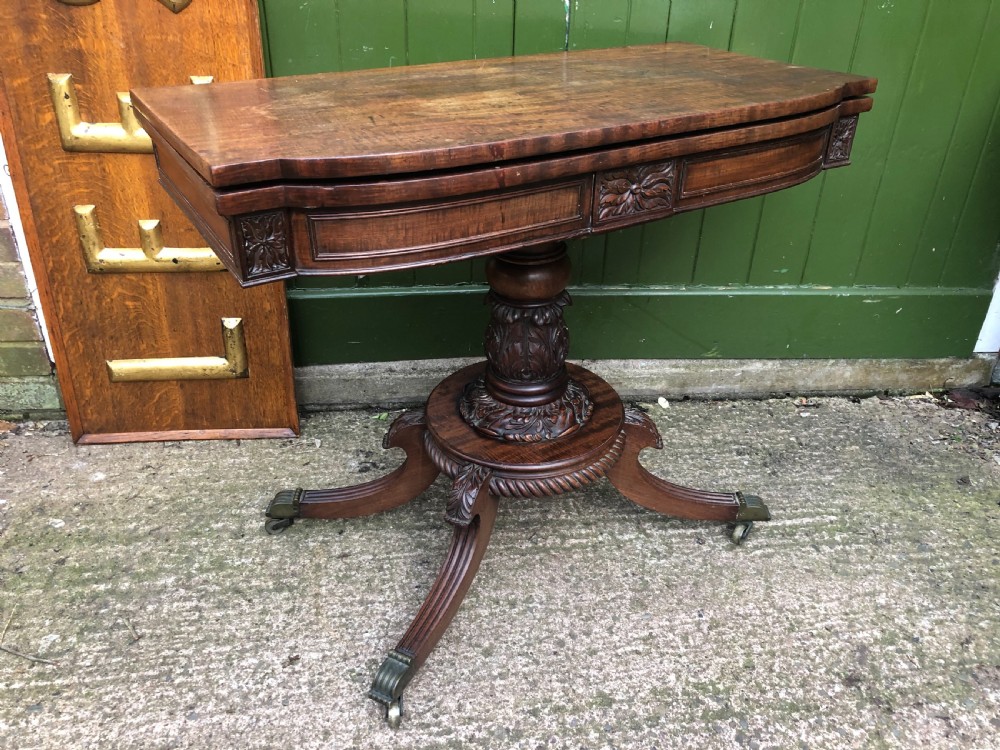 An early 19th-century Regency mahogany fold-over card table featuring carved floral frieze panels, a bulbous carved pedestal stem, and four splayed legs with brass castors. View XVIII