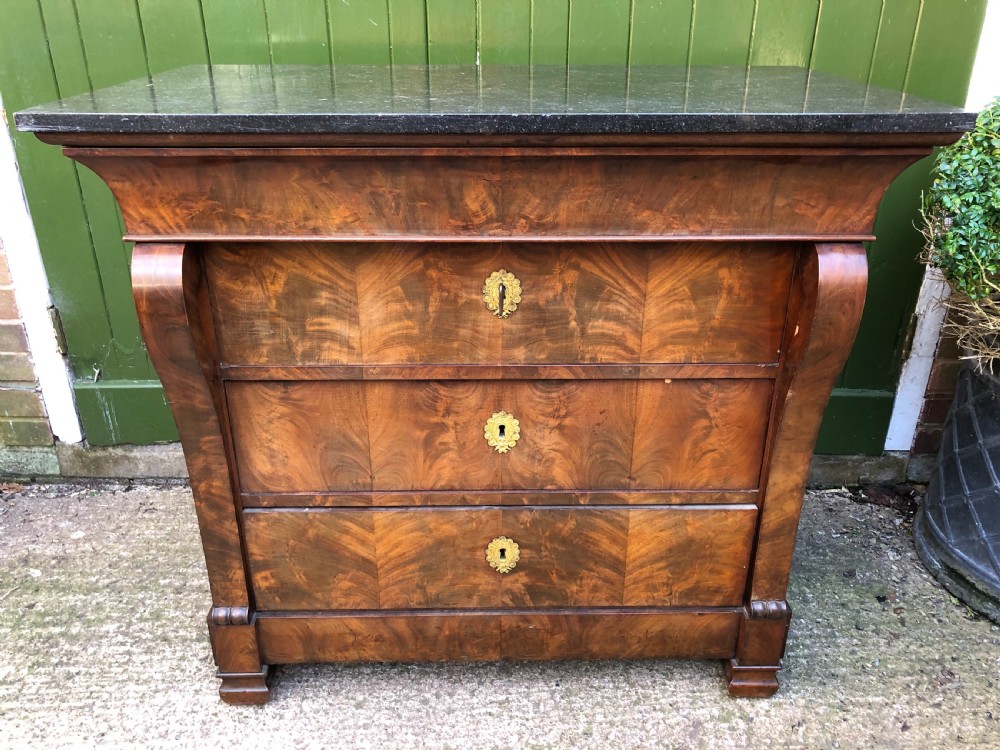 An early nineteenth-century French Empire mahogany commode featuring three drawers with flame mahogany veneer, brass escutcheons, and a thick dark fossil marble top. View V