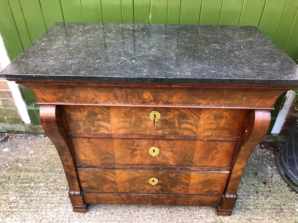 An early nineteenth-century French Empire mahogany commode featuring three drawers with flame mahogany veneer, brass escutcheons, and a thick dark fossil marble top. View VI