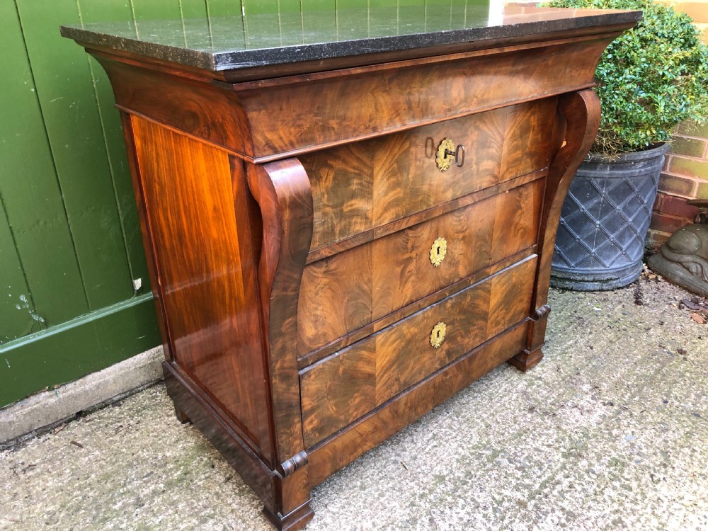An early nineteenth-century French Empire mahogany commode featuring three drawers with flame mahogany veneer, brass escutcheons, and a thick dark fossil marble top. View VIII