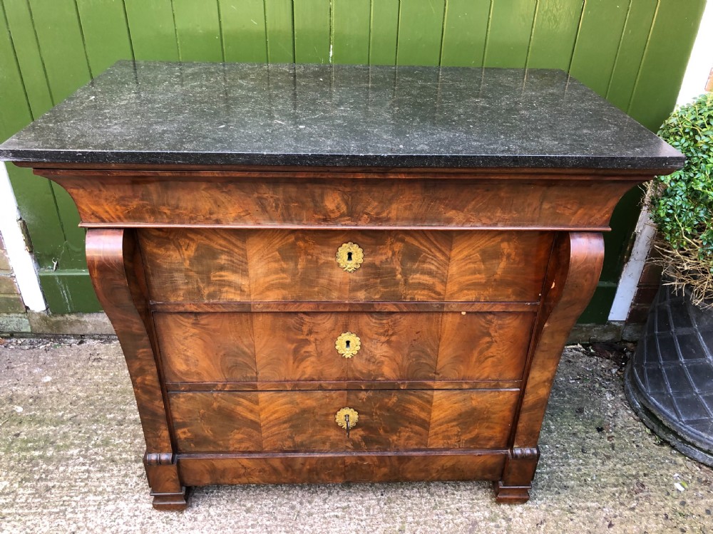 An early nineteenth-century French Empire mahogany commode featuring three drawers with flame mahogany veneer, brass escutcheons, and a thick dark fossil marble top. View X
