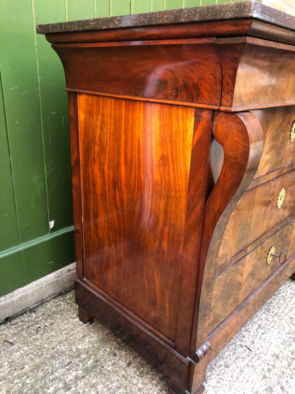 An early nineteenth-century French Empire mahogany commode featuring three drawers with flame mahogany veneer, brass escutcheons, and a thick dark fossil marble top. View XI