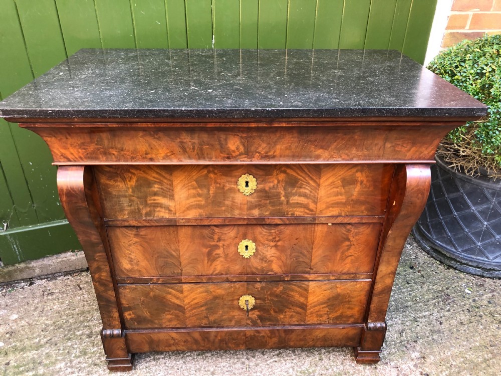 An early nineteenth-century French Empire mahogany commode featuring three drawers with flame mahogany veneer, brass escutcheons, and a thick dark fossil marble top. View XV