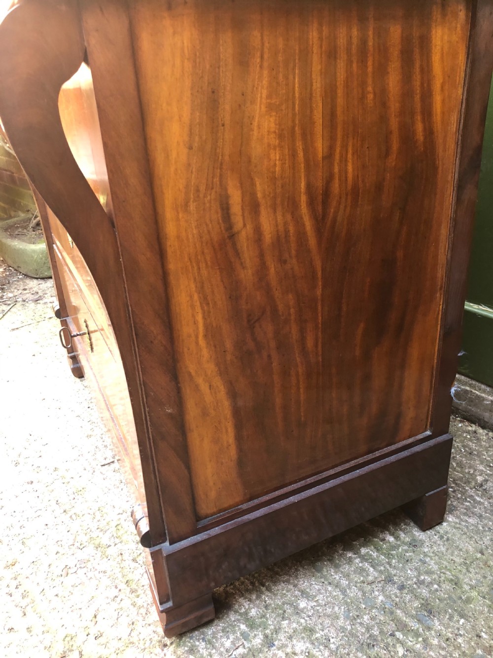 An early nineteenth-century French Empire mahogany commode featuring three drawers with flame mahogany veneer, brass escutcheons, and a thick dark fossil marble top. View XVI