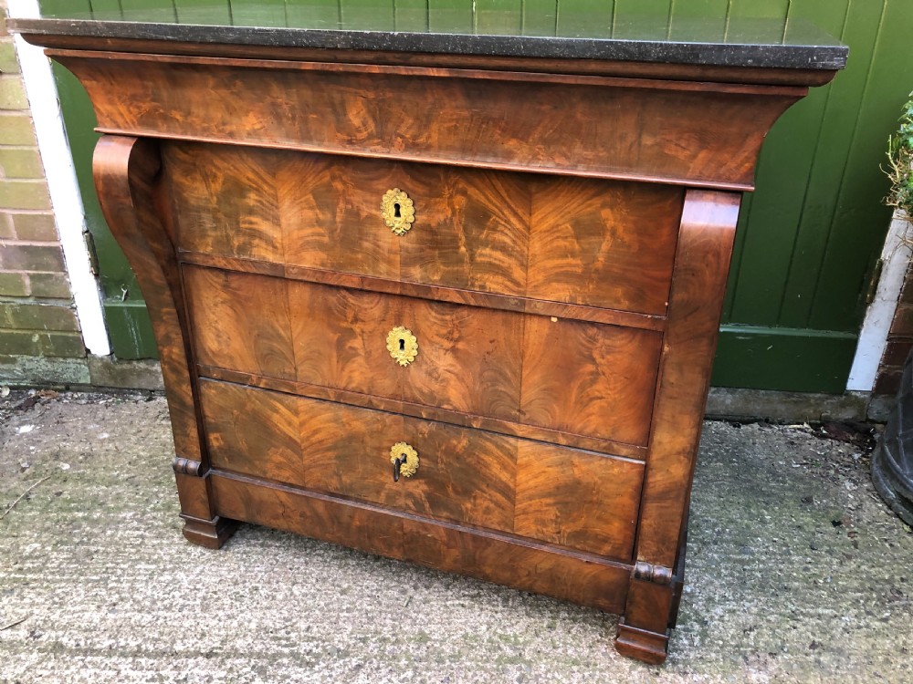 An early nineteenth-century French Empire mahogany commode featuring three drawers with flame mahogany veneer, brass escutcheons, and a thick dark fossil marble top. View XVII