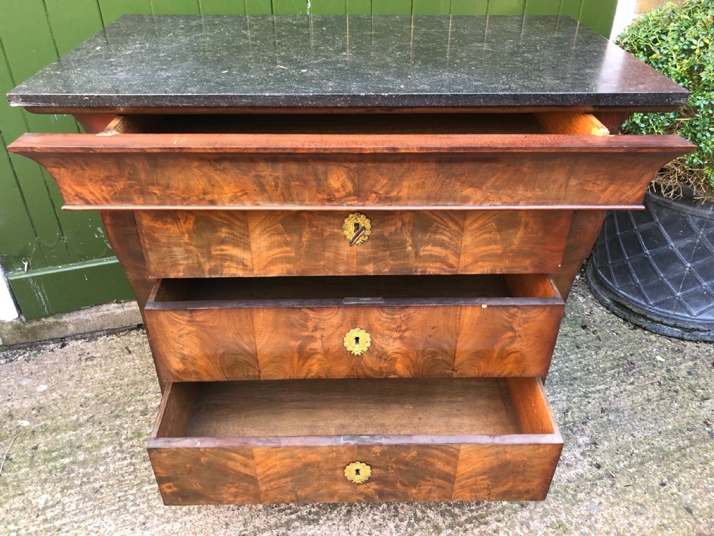An early nineteenth-century French Empire mahogany commode featuring three drawers with flame mahogany veneer, brass escutcheons, and a thick dark fossil marble top. View XIX