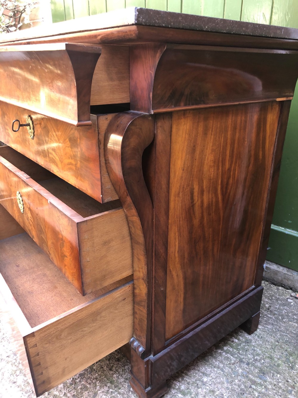 An early nineteenth-century French Empire mahogany commode featuring three drawers with flame mahogany veneer, brass escutcheons, and a thick dark fossil marble top. View XX
