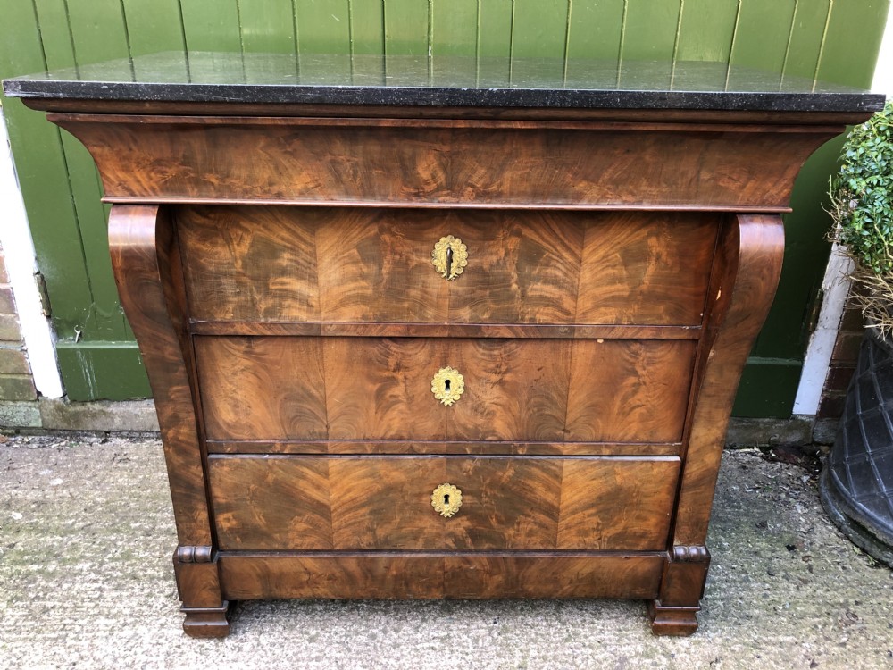 An early nineteenth-century French Empire mahogany commode featuring three drawers with flame mahogany veneer, brass escutcheons, and a thick dark fossil marble top.