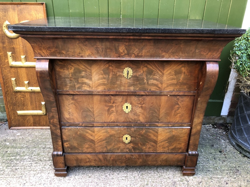 An early nineteenth-century French Empire mahogany commode featuring three drawers with flame mahogany veneer, brass escutcheons, and a thick dark fossil marble top. View XXV