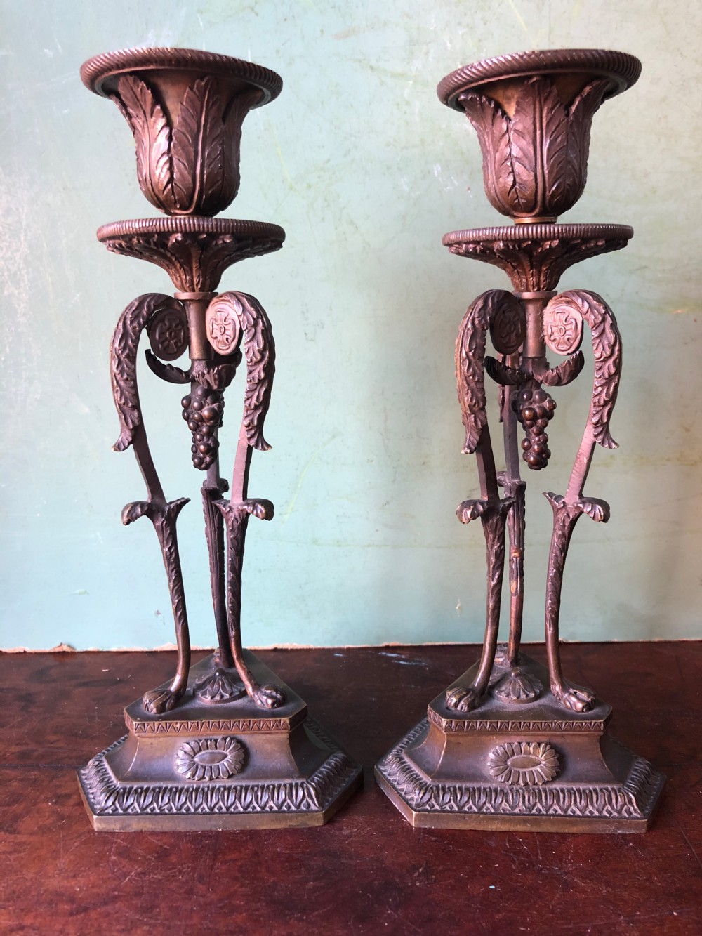 A pair of early nineteenth-century Regency bronze candlesticks designed in classical Athenienne tripod form with leaf sconces and plinth bases.