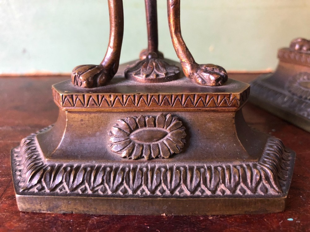 A pair of early nineteenth-century Regency bronze candlesticks designed in classical Athenienne tripod form with leaf sconces and plinth bases. View VI