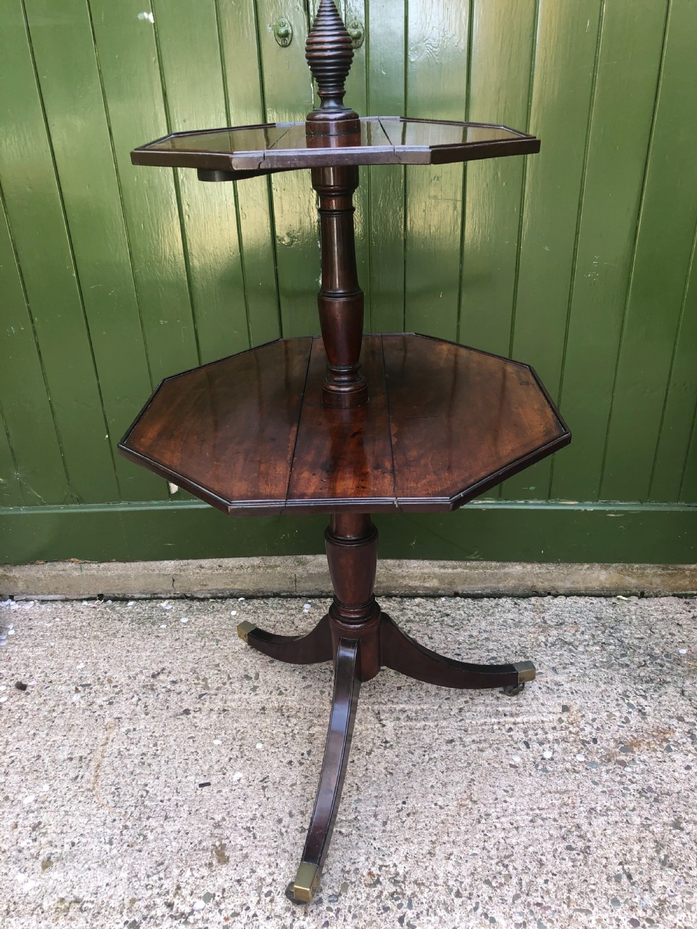 A late eighteenth-century George III mahogany two-tier dumb waiter table featuring octagonal drop-leaf surfaces supported by a turned central column on tripod legs with brass castors.