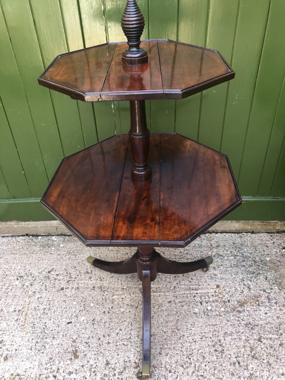 A late eighteenth-century George III mahogany two-tier dumb waiter table featuring octagonal drop-leaf surfaces supported by a turned central column on tripod legs with brass castors. View II