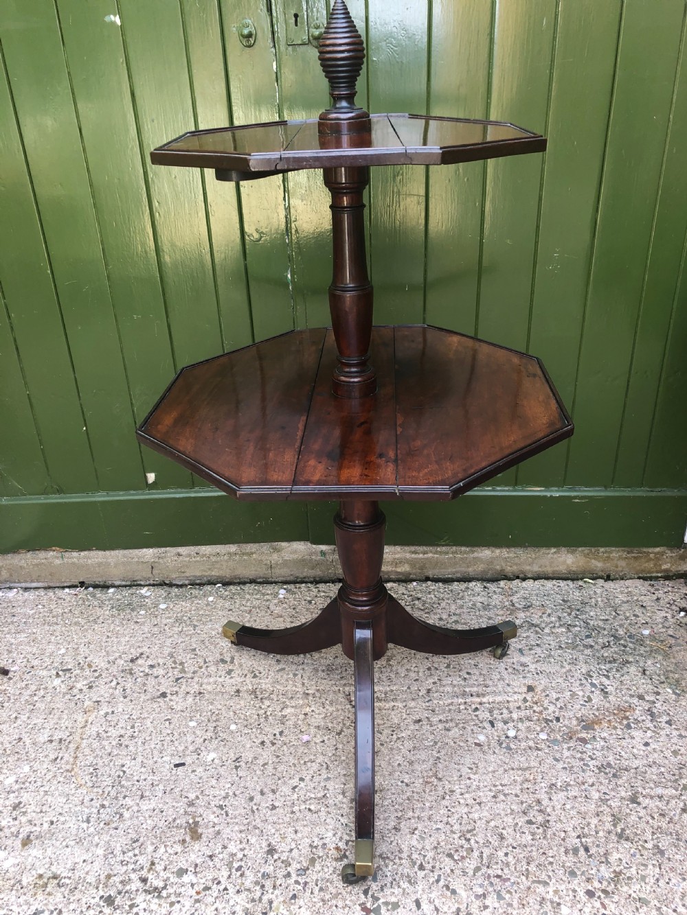 A late eighteenth-century George III mahogany two-tier dumb waiter table featuring octagonal drop-leaf surfaces supported by a turned central column on tripod legs with brass castors. View III