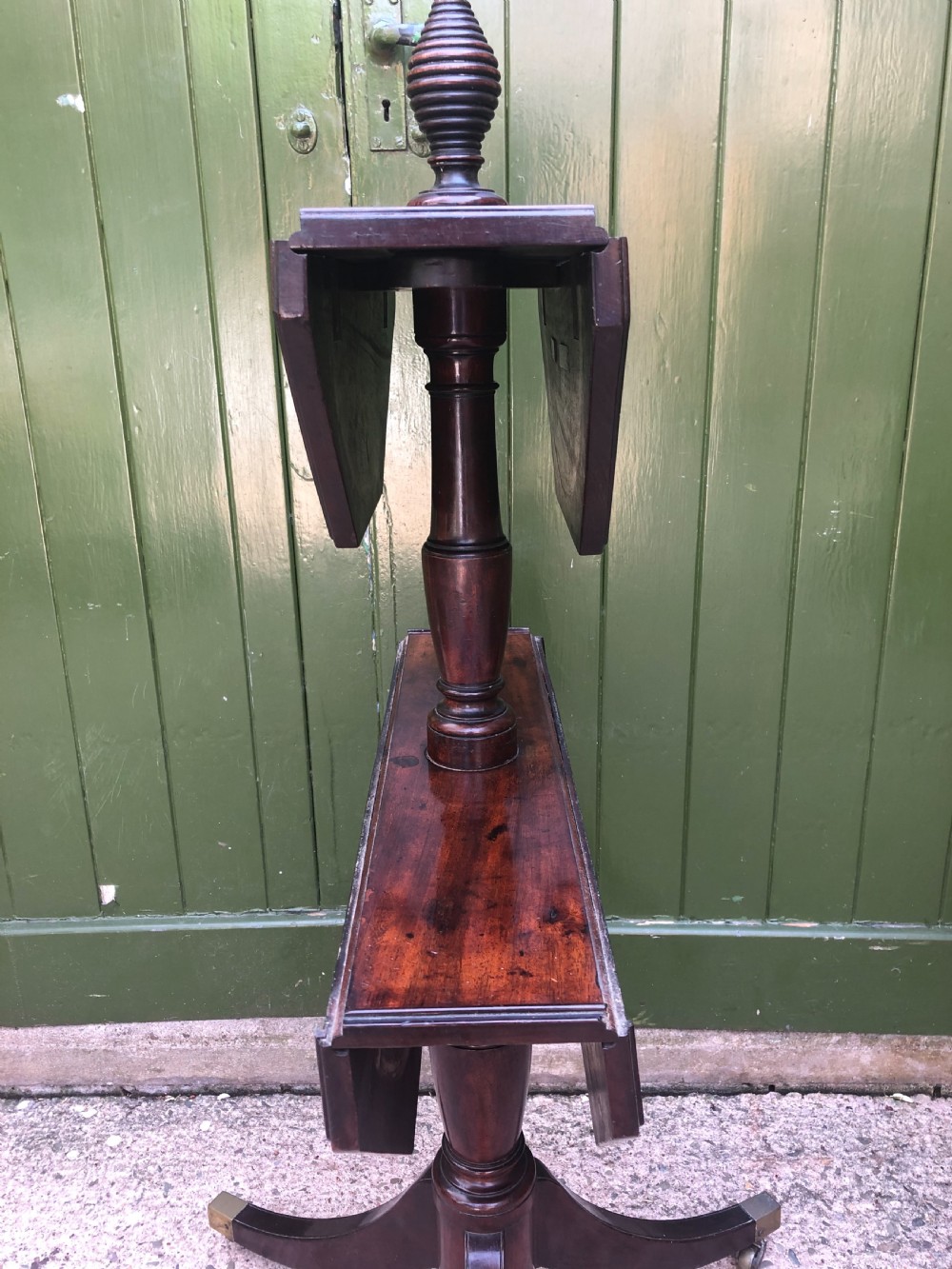 A late eighteenth-century George III mahogany two-tier dumb waiter table featuring octagonal drop-leaf surfaces supported by a turned central column on tripod legs with brass castors. View XII