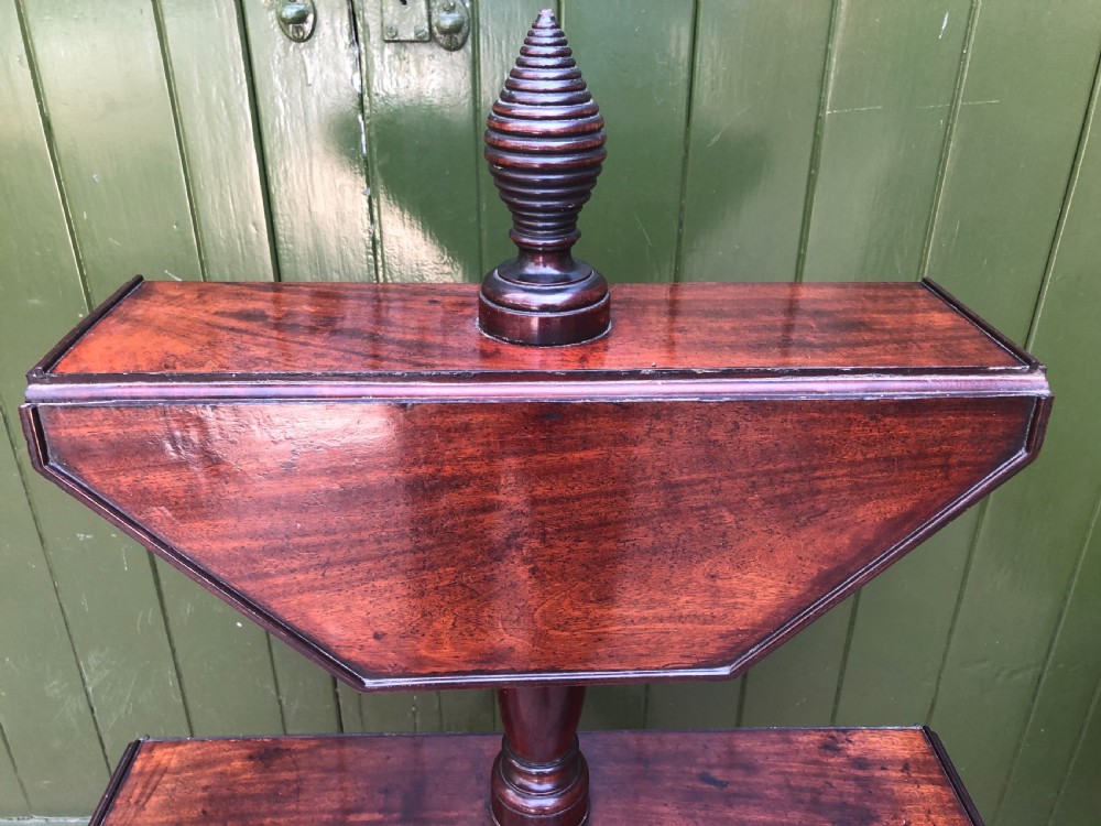 A late eighteenth-century George III mahogany two-tier dumb waiter table featuring octagonal drop-leaf surfaces supported by a turned central column on tripod legs with brass castors. View XV