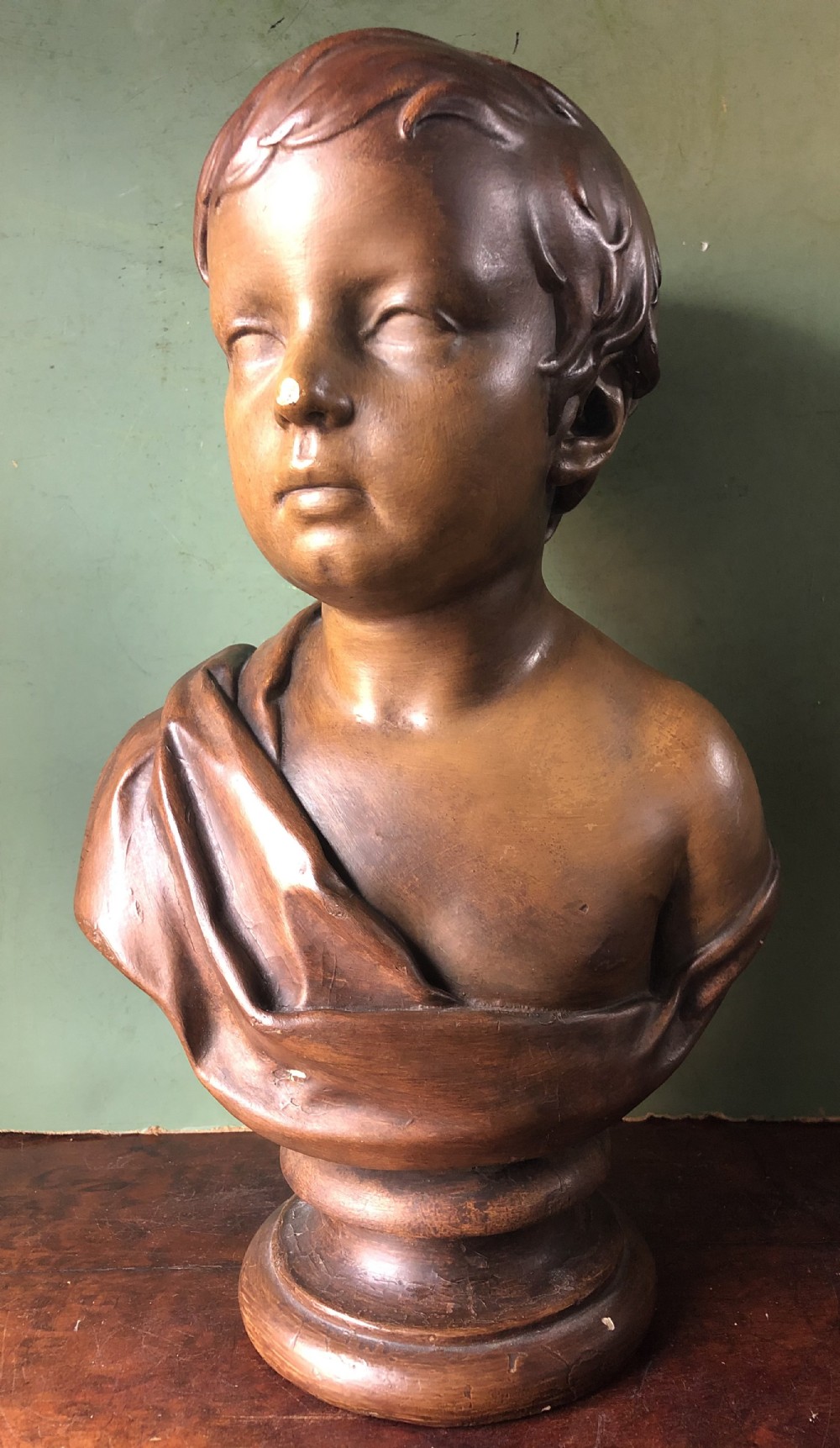 An early nineteenth-century patinated plaster bust of a young boy with draped shoulder fabric, set on a turned circular pedestal base.