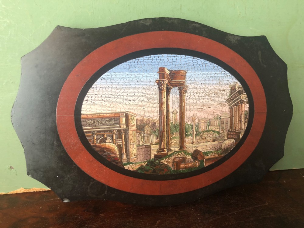 A cartouche-shaped black marble paperweight with a terracotta-coloured inlay ring surrounding a central oval micro-mosaic depicting classical Roman architectural ruins. View II