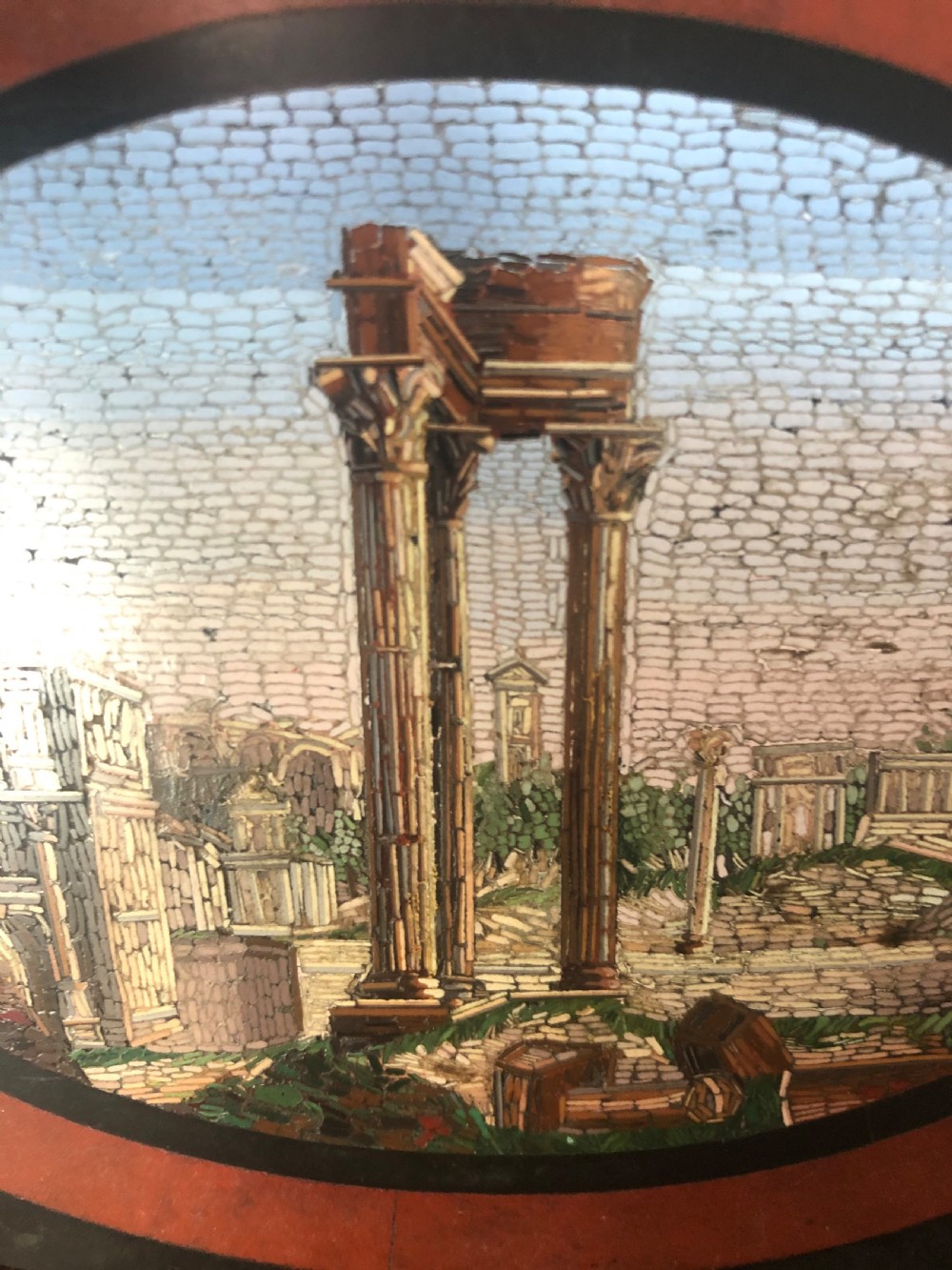 A cartouche-shaped black marble paperweight with a terracotta-coloured inlay ring surrounding a central oval micro-mosaic depicting classical Roman architectural ruins. View III