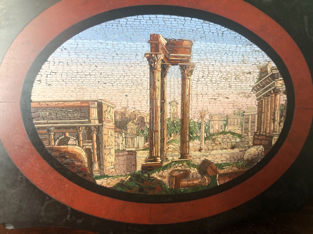 A cartouche-shaped black marble paperweight with a terracotta-coloured inlay ring surrounding a central oval micro-mosaic depicting classical Roman architectural ruins. View IV